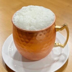 Frothy Yogurt Drink Served In Hammered Copper Mug On Wooden Table Surface